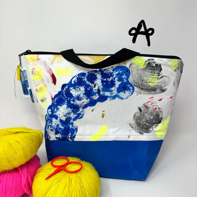 Tote bag with colorful design next to yarn and scissors on a white background