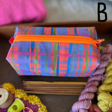 Load image into Gallery viewer, Colorful plaid fabric pouch with an orange zipper on a surface with yarn and crochet items.
