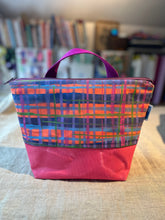 Load image into Gallery viewer, Colorful plaid bag with a pink base on a textured surface with books in the background
